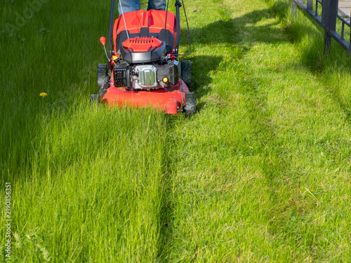 A man with a lawnmower is mowing the grass in a close‑up
