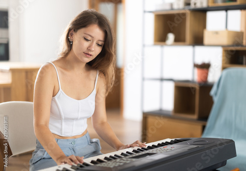 Принти на полотні Young woman wears shorts, sits at synthesizer and plays music in room