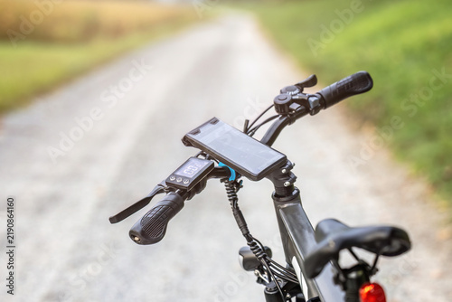 Close-up of an e-bike handlebar with GPS smartphone mount on a gravel path during a cycling trip in rural countryside.