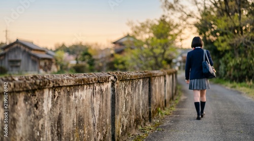 Japanese high school girl walking on a vintage rural road in nostalgic sunset