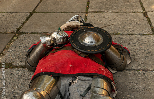 Obraz na płótnie Fallen knight in full steel armor and red tunic lying on ground holding round sh