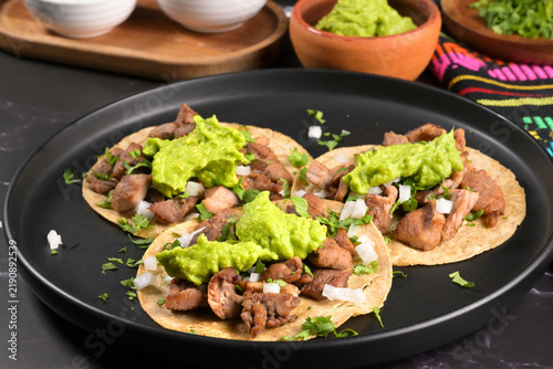 Mexican food. Street style pork tacos with guacamole and authentic textiles on a dark surface