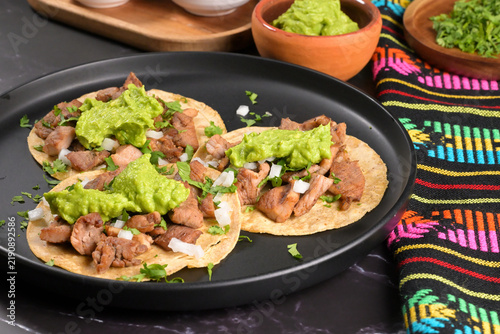 Tasty Mexican dish of pork street tacos with classic toppings and vibrant traditional napkin in the background