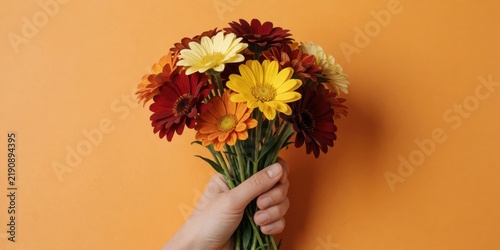 A person holding a vibrant bouquet of colorful autumn gerbera daisies against a solid orange background for floral design and greeting concepts