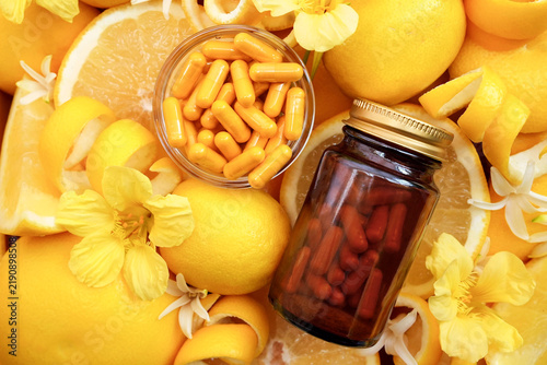Fotografie Yellow pills on bright citrus fruits background, bottle of vitamin C, natural me