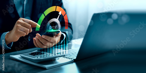 Financial risk assessment concept with business professional using smartphone beside laptop showing virtual risk gauge, rising chart, calculator and corporate decision analysis