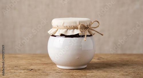 White ceramic jar with jam and fabric lid on wooden table