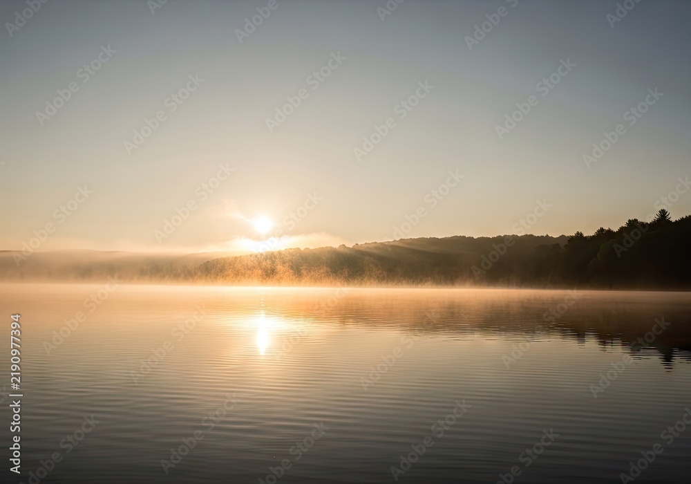 Fototapeta premium Golden sun reflecting on misty lake surface.