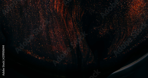 Ink spill. Sparkling fluid. Defocused orange golden color glitter mix acrylic texture floating on abstract art dark background.