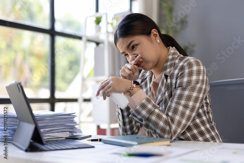 Asian businesswoman blowing her nose while working in office.
