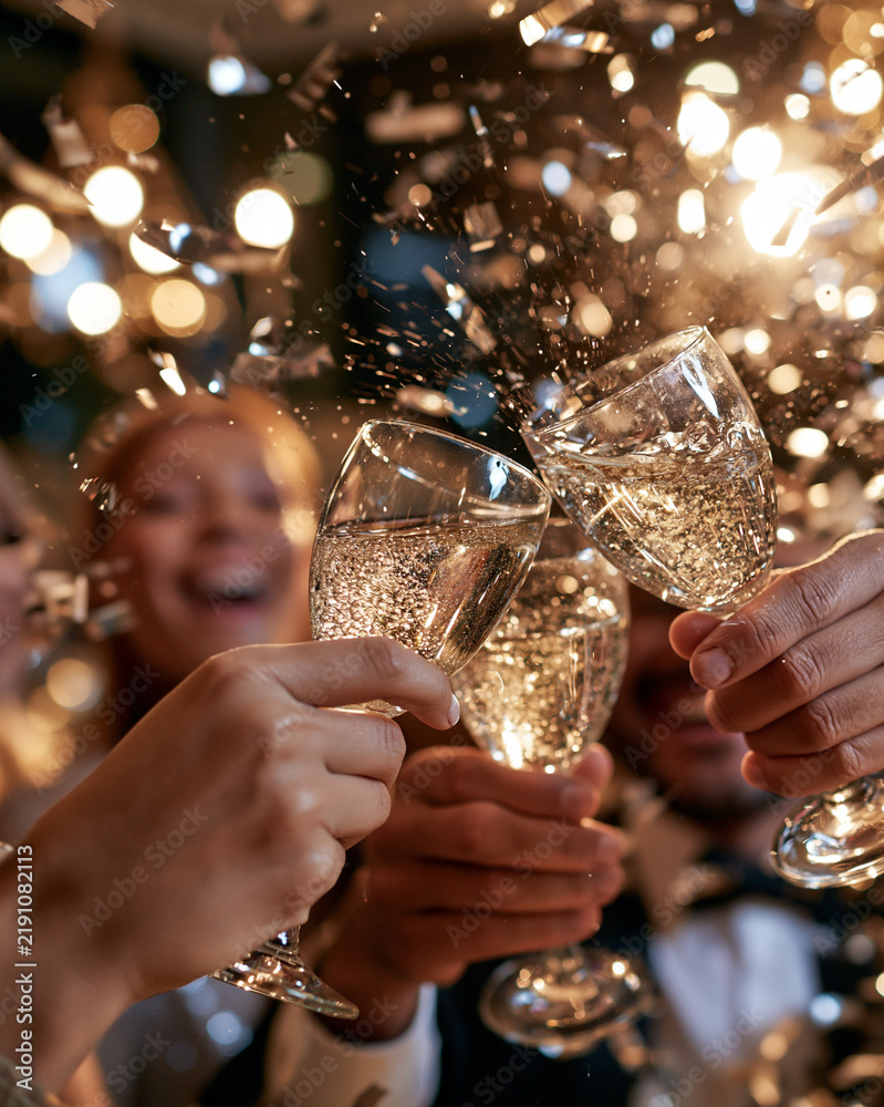 Obraz premium Golden confetti swirls around clinking champagne flutes. Joyful hands toast with sparkling glasses against warm lights. Celebrations buzz with laughter and sparkling joy. Perfect for birthdays