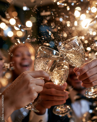 Golden confetti swirls around clinking champagne flutes. Joyful hands toast with sparkling glasses against warm lights. Celebrations buzz with laughter and sparkling joy. Perfect for birthdays