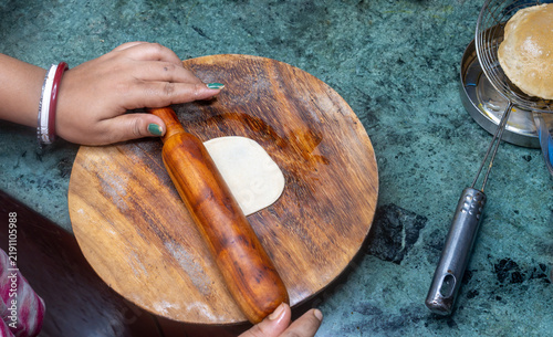 Obraz na płótnie Indian woman's hands rolling a small whole wheat puri dough on a traditional rolling board using a wooden rolling pin at home on kitchen background