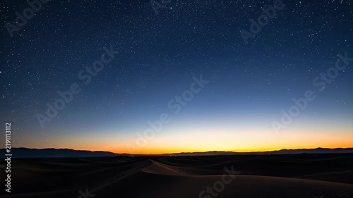 Starry Night Sky Over Desert Dunes At Twilight With Distant Horizon Lights