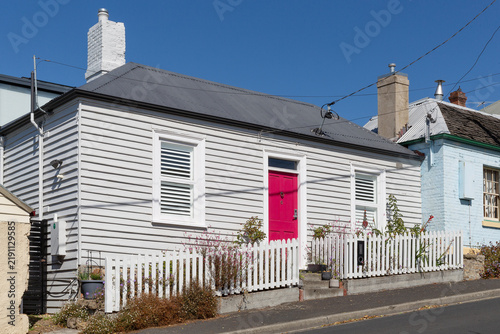 Weatherboard cottage painted grey with a bright red front door and a white picket fence