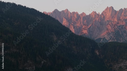 Drone view of a high mountain range in the morning, with mountain peaks illuminated by the red glow of the rising sun, captured with a telephoto lens.