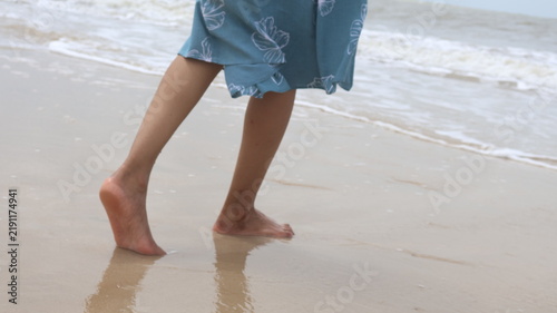 фотографія A woman's legs and bare feet as she walks on a beach, water swirling around her ankles, embodying summer bliss and escape
