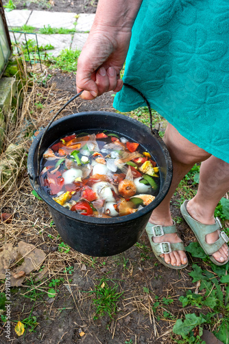 A person is holding a bucket of food waste for composting in the garden.