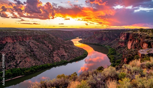 Sunset Over a Scenic River and Mountain Landscape with Reflections on Calm Water and Dramatic Clouds in Nature at Golden Hour