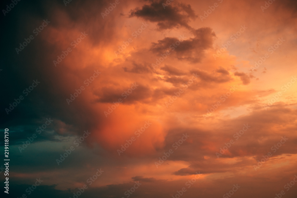 Fototapeta premium Dramatic storm clouds glowing orange and red beneath intense evening light, with dark turbulent formations creating a powerful atmospheric sky.