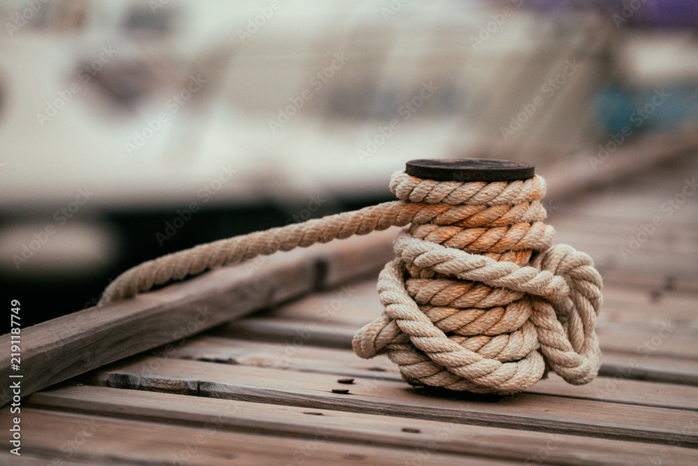 Obraz premium Close-up of a thick nautical mooring rope securely wrapped around a metal bollard on a wooden pier.