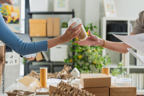 Fotografie Caring Asian entrepreneur handing takeaway coffee cup to coworker at sustainable