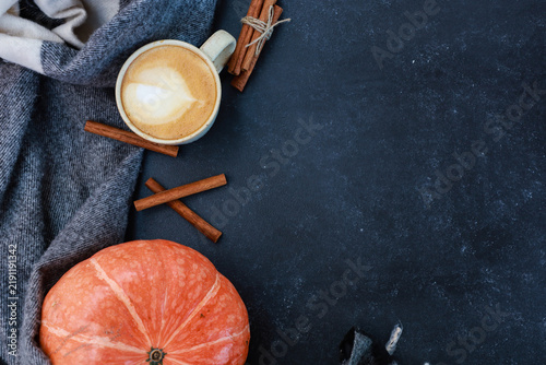 Cup of tasty coffee, spices and bright orange pumpkin with gray scarf on dark table. Top view with copy space. Autumn hot drink, coffee shop menu, thanksgiving time concept
