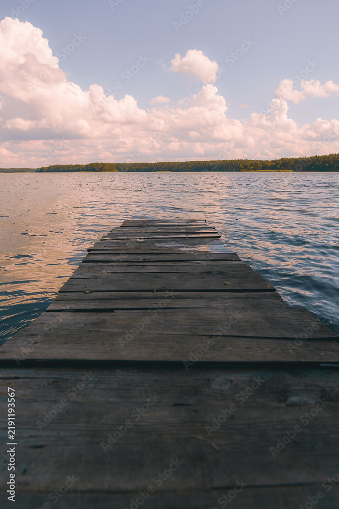 Fototapeta premium Wooden jetty on water with scenic clouds