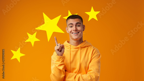 Quadro su tela Young man points at yellow stars on orange background during a cheerful moment