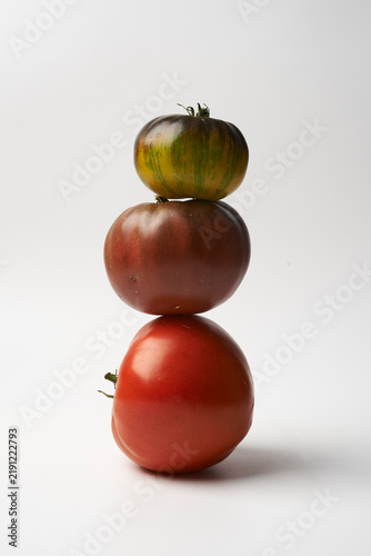 Three colorful heirloom tomatoes stacked on top of each other against a white background, still life food photography
