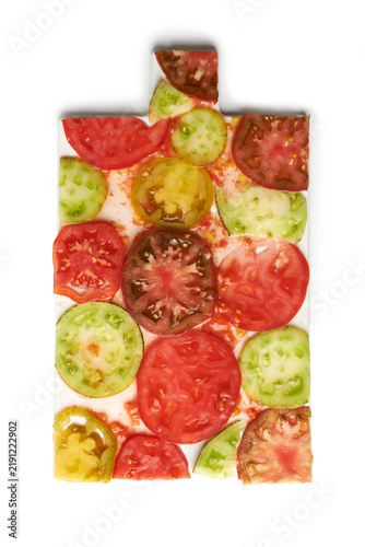 Colorful heirloom tomato slices of different varieties arranged in a pattern on a white cutting board, top view food photography