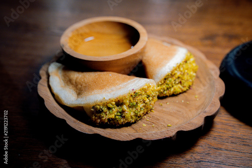 Traditional Arab qatayef pancakes folded around a pistachio filling and served with sweet syrup on a wooden plate.