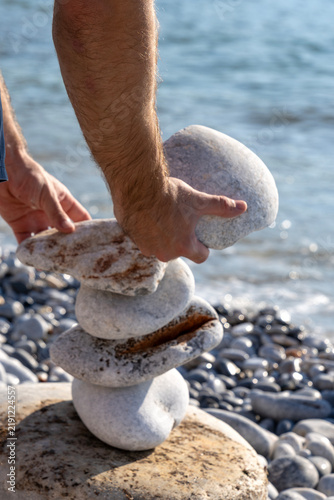 Photography Close-up of hands building stone balance pyramid on beach