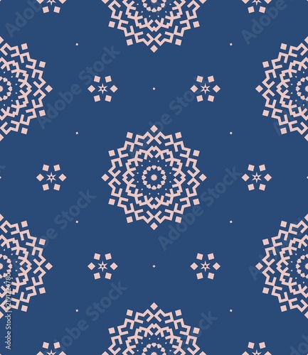 Geometric patterns form a symmetrical design. Light-colored motifs repeat across a deep blue background. Each shape radiates from a central point. Patterns resemble stylized flowers or mandalas