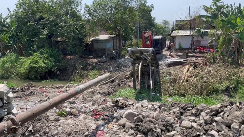 Orange excavator dismantling concrete structure near village river bank