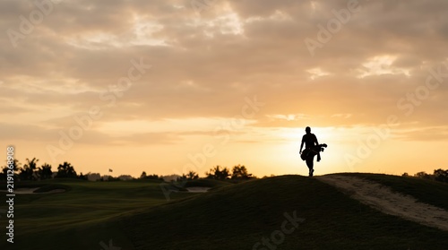 Golfer silhouette walking on course at sunset evening sky