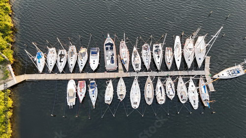 Foto Yachthafen mit dicht an dicht liegenden Segelbooten am Holzsteg, aufgenommen aus der Luft bei ruhigem Licht und dunklem Wasser