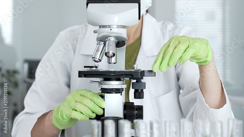 Obraz na płótnie Female scientist wearing a lab coat and safety glasses working with a microscope