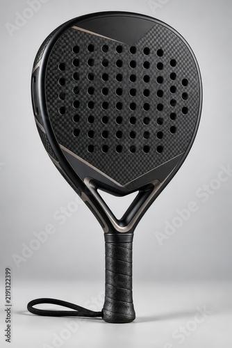 High-quality black padel racket with visible carbon fiber texture and perforated face, standing upright on a seamless gray backdrop, ideal for sports product photography.