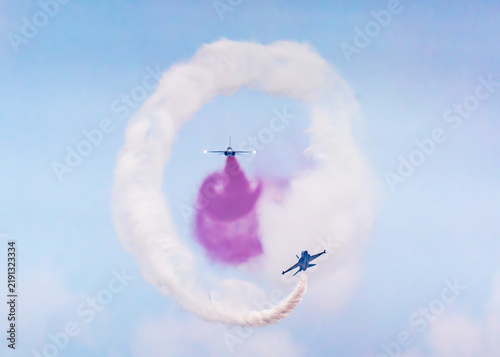 Aerial view of Korea Black Eagles fighter jets performing a synchronized aerial maneuver with white and purple smoke trails against a clear blue sky at the Changi Exhibition Centre, Singapore.