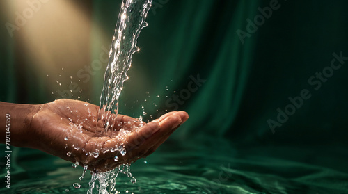 Water pouring on dark hand in dark setting, with splashing droplets and reflective surface conveying freshness, renewal, and careful hydration