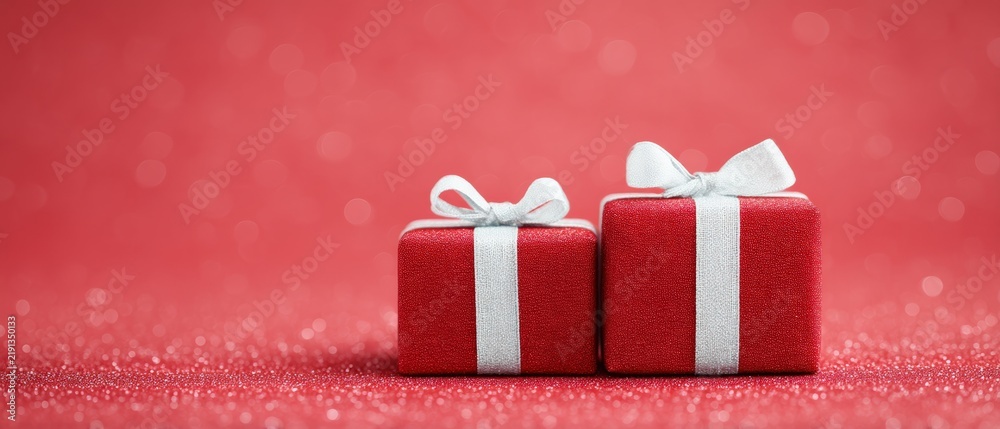 Obraz premium Bright red gift boxes adorned with white ribbons set against a shimmering background ideal for holiday festivities and memorable events inspiring happiness and excitement for the arrival of gifts
