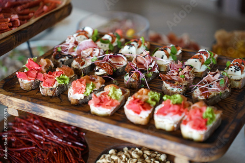Variety of festive appetizers on wooden trays, including canapes, cured meats, nuts, vegetables and fresh greens.