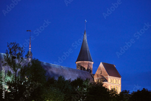 Foto Illuminated Konigsberg cathedral spire and roof under deep blue evening sky in K