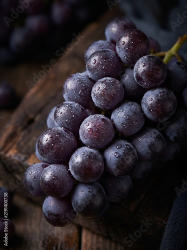 Fresh bunch of purple grapes with water droplets on rustic wood
