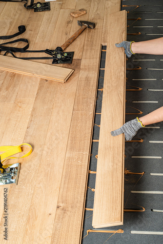 Worker installing parquet wooden plank over acoustic underlayment with applied adhesive