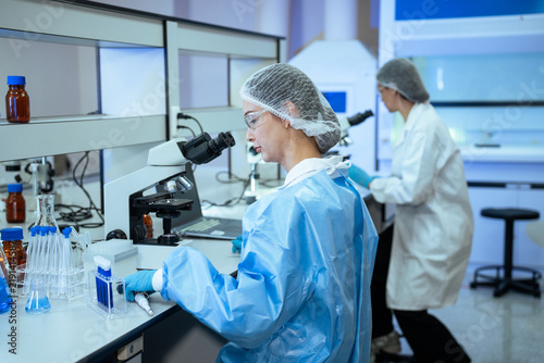 A team of researchers conducts medical tests and analyzes chemical samples using microscopes and lab equipment inside a clean laboratory facility during daytime work hours.