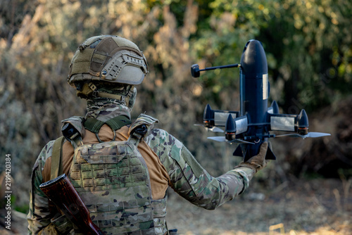 Obraz na plátně A soldier in a helmet, holding an assault rifle and an anti-aircraft drone