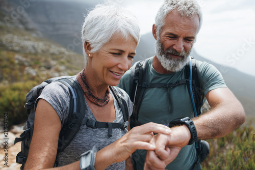 Happy senior Caucasian couple checking smartwatch route together during outdoor hike