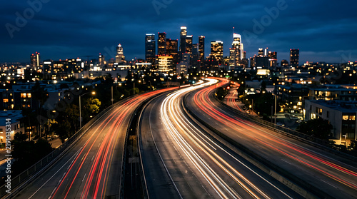 Nighttime city skyline with illuminated high-rise buildings and streaks of vehicle lights on a curving highway